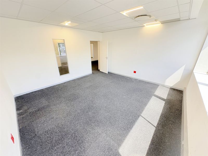 A bright, vacant office space featuring neutral carpet flooring, a suspended ceiling with recessed lighting, and an internal glass panel.