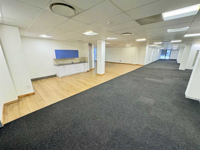 Spacious open-plan office area featuring a kitchenette, suspended ceilings with recessed lighting, and a combination of carpet and laminate flooring.