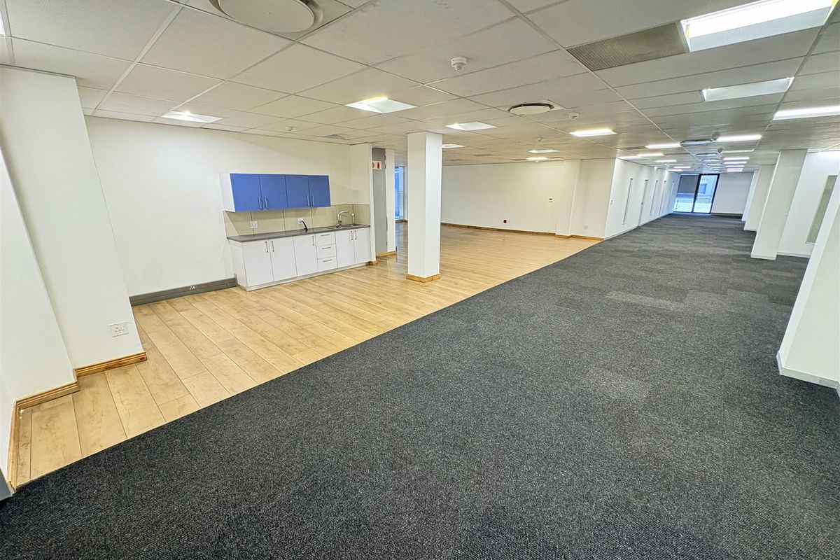 Spacious open-plan office area featuring a kitchenette, suspended ceilings with recessed lighting, and a combination of carpet and laminate flooring.