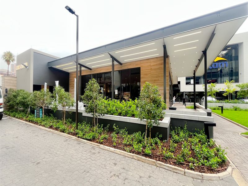 Modern office building exterior featuring a sleek facade, large glass windows, integrated LED lighting, and well-maintained landscaped planter boxes.
