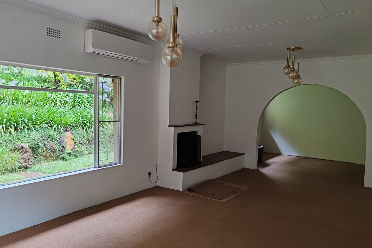 Spacious living area featuring a built-in fireplace, wall-mounted air conditioning unit, and an arched entryway leading to an adjacent room.