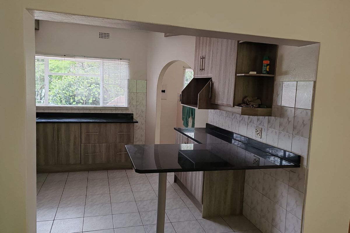 A functional kitchen featuring wood-look cabinetry, dark granite countertops, a breakfast bar, and tiled flooring with a view through the window.