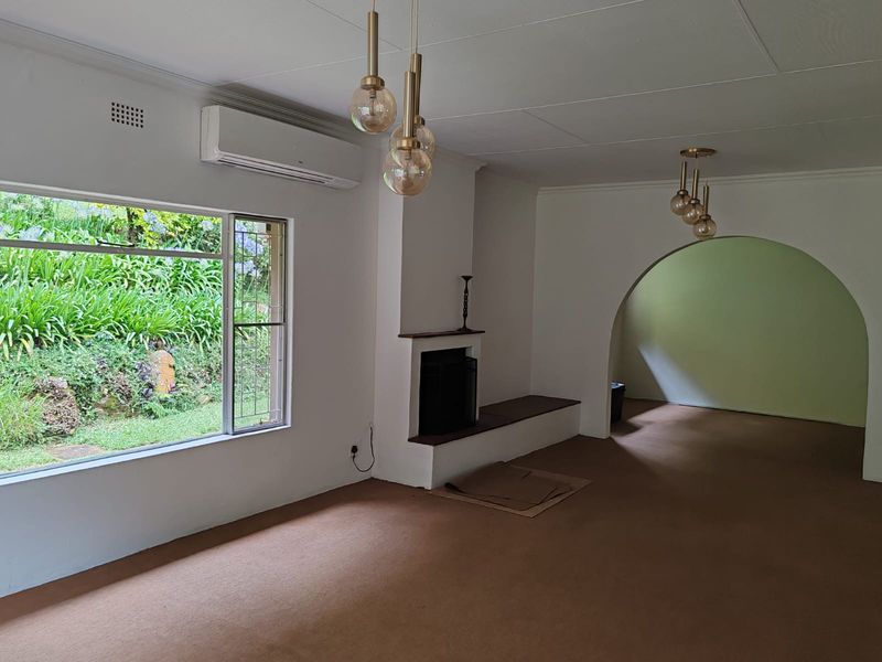 Spacious living area featuring a built-in fireplace, wall-mounted air conditioning unit, and an arched entryway leading to an adjacent room.