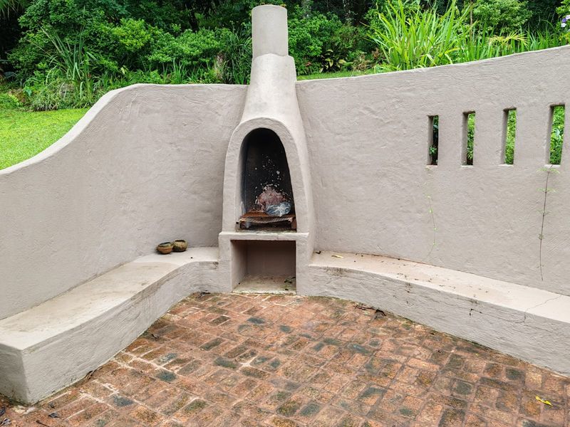 Outdoor entertainment area featuring a built-in masonry fireplace with integrated bench seating and brick paved flooring set within a garden landscape.