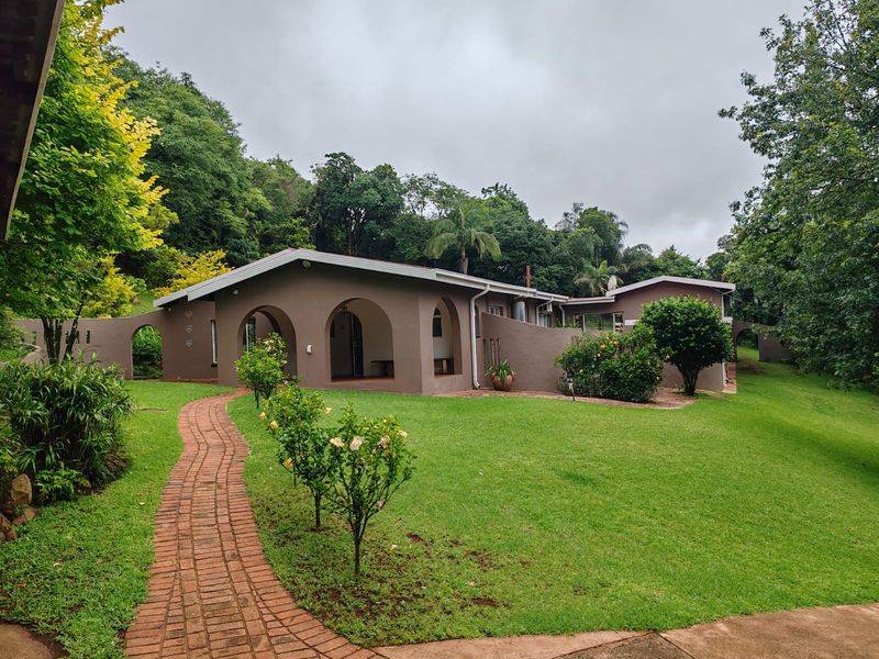A view of the rear exterior of the farm property, featuring a covered patio with arched architectural details, brick pathway, and landscaped garden.