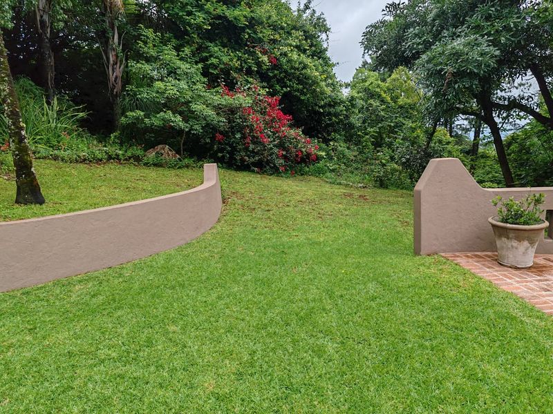 A well-maintained garden area featuring curved retaining walls, lush green lawn, and mature trees, providing a peaceful outdoor space on the farm property.
