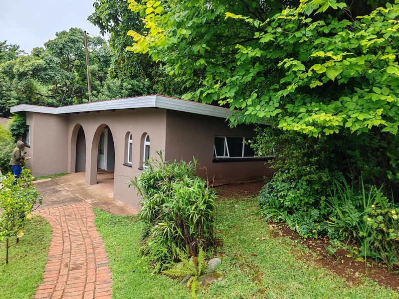 A view of the farm property exterior featuring a covered patio with arched architectural details, brick pathway, and surrounding mature garden landscaping.