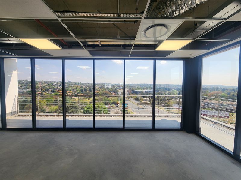 Unfinished open-plan office space featuring floor-to-ceiling windows, access to a private balcony, and an exposed ceiling grid with recessed lighting.