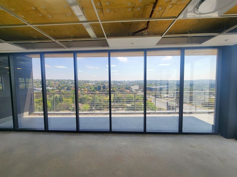Unfinished office space featuring floor-to-ceiling glass doors leading to a balcony with expansive suburban views and an exposed ceiling structure.