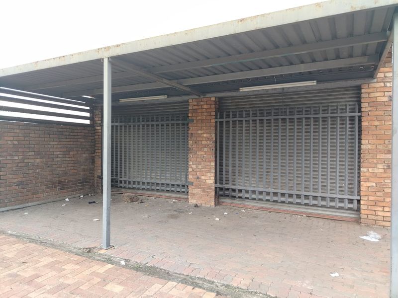 A covered commercial garage or parking area featuring brick walls, secure metal roller shutters, and paved flooring.