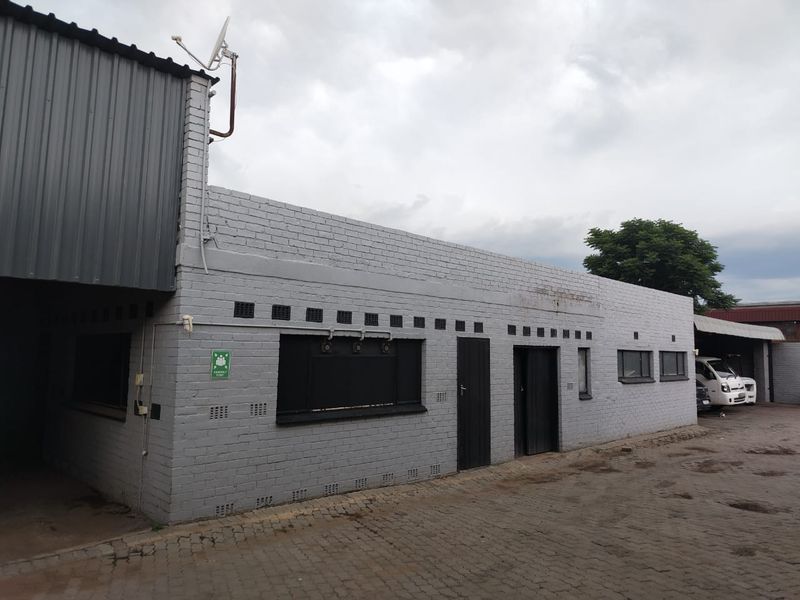 Commercial property exterior featuring a painted brick facade, corrugated metal roof section, and paved driveway access.