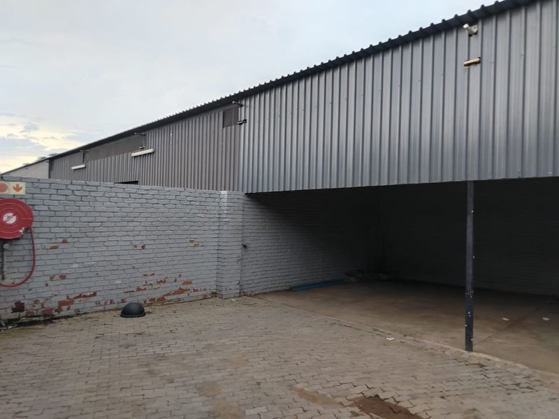 Rear exterior view of a commercial warehouse featuring corrugated metal siding, a painted brick boundary wall, and a paved loading or parking area.