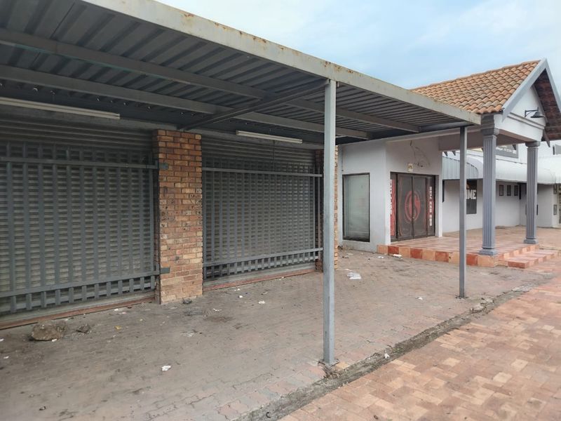 Commercial storefront exterior featuring a metal canopy, brick support pillars, and security roller shutters over the entrance.