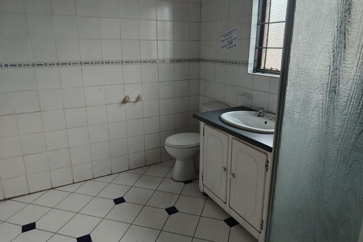A functional bathroom featuring a vanity cabinet with a basin, toilet, and tiled finishes throughout, requiring minor cosmetic updates.