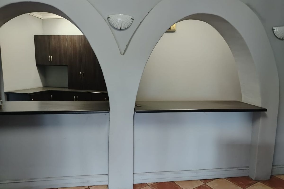 A kitchen area featuring a distinctive double-arch serving counter, dark built-in cabinetry, and tiled flooring, offering a functional layout for commercial use.