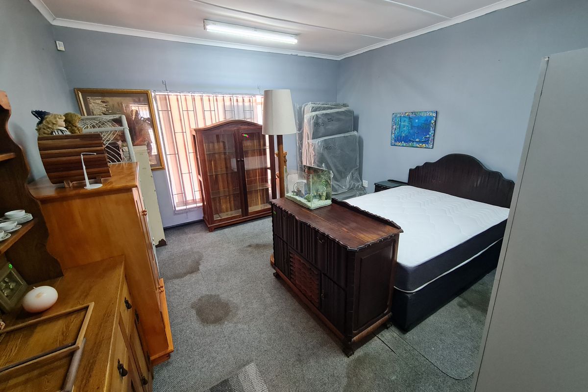 A bedroom featuring grey walls, carpeted flooring, and vertical window blinds, currently utilized for storage.