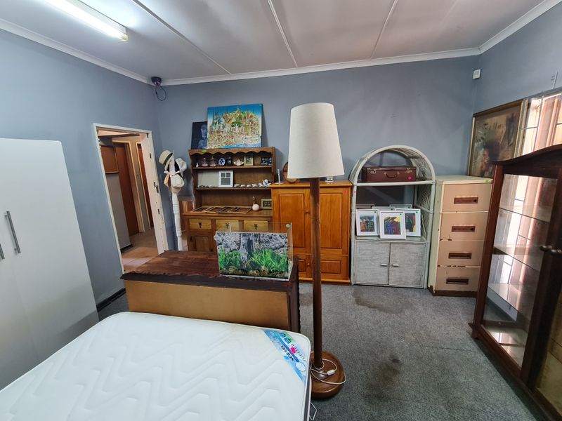 A bedroom space featuring grey walls, carpeted flooring, and a fluorescent ceiling light fixture, currently used for storage.