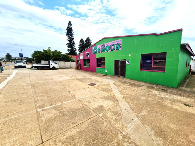Front exterior view of a retail property featuring a large paved parking area and a prominent building facade with security gate access.