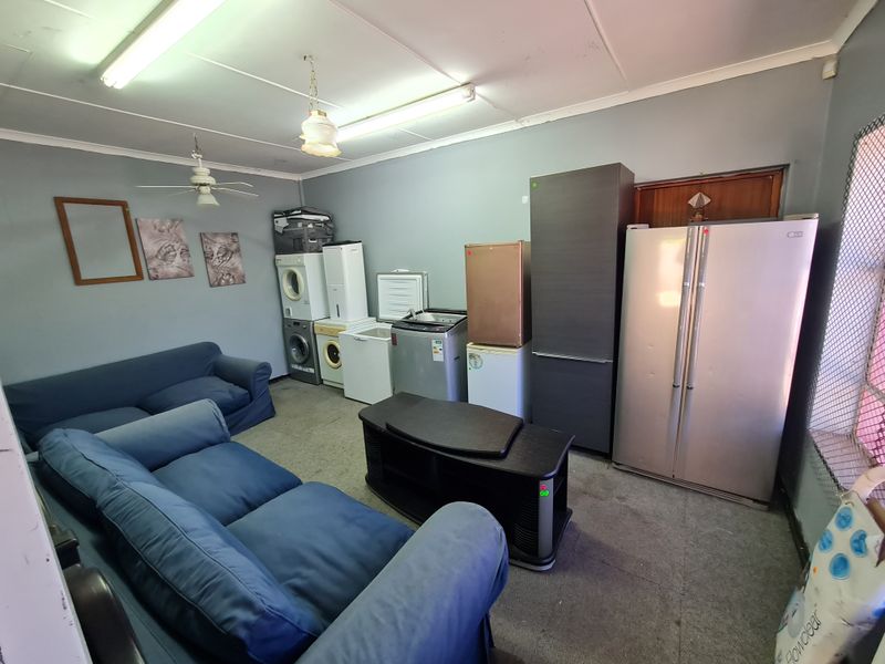 A utility space featuring fluorescent lighting and a ceiling fan, currently utilized for storage and appliance placement.