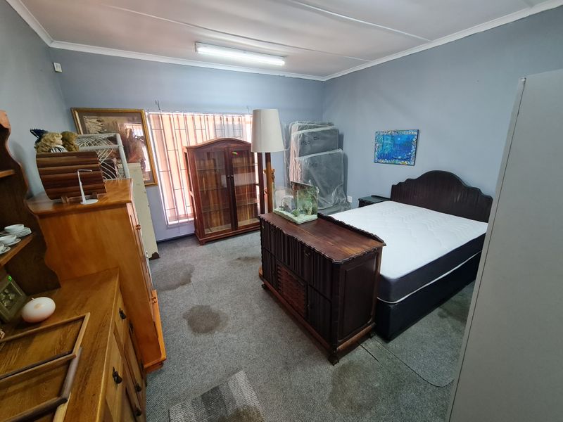 A bedroom featuring grey walls, carpeted flooring, and vertical window blinds, currently utilized for storage.