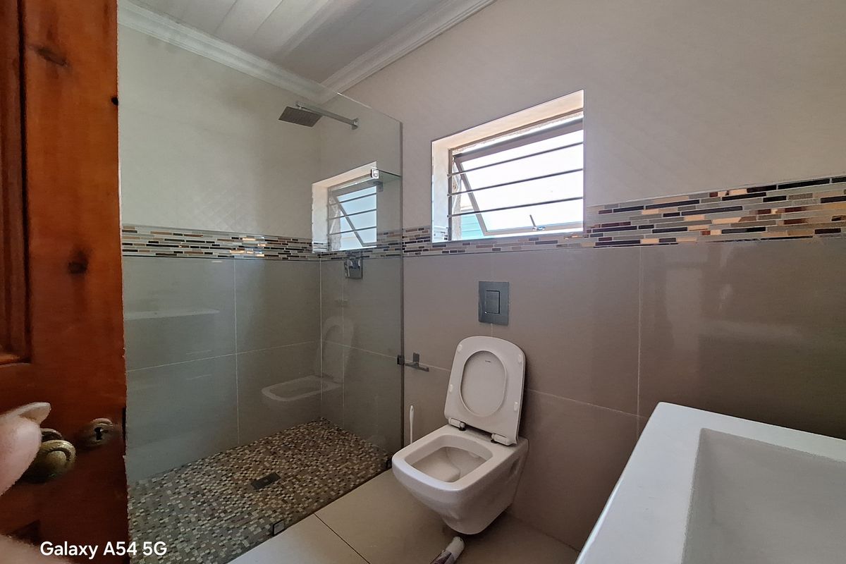 Modern bathroom featuring a walk-in shower with glass enclosure, pebble-tiled floor, wall-mounted toilet, and decorative mosaic tile border.