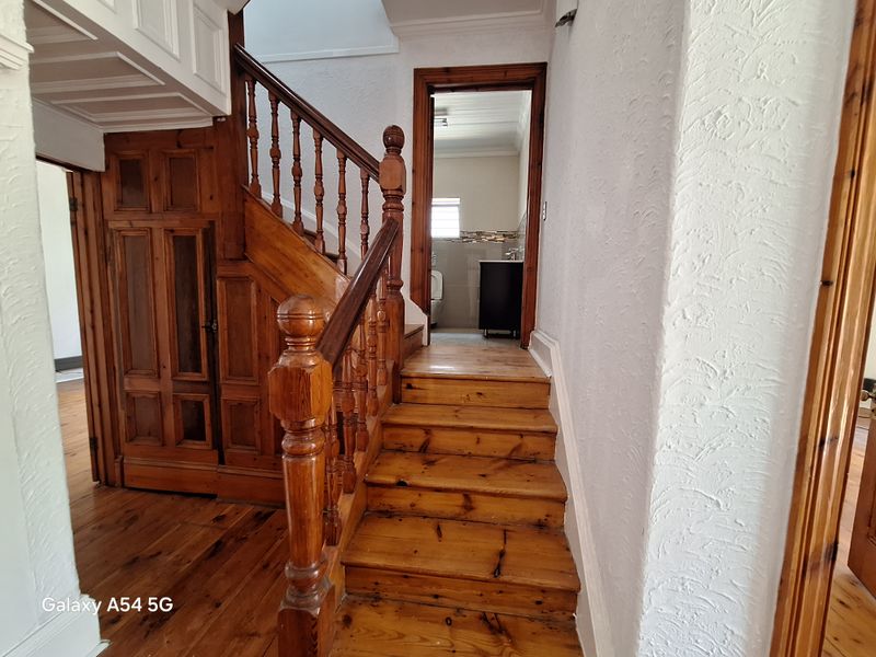 A traditional wooden staircase with ornate balustrades leading to an upper level, with a view into an adjacent bathroom area.
