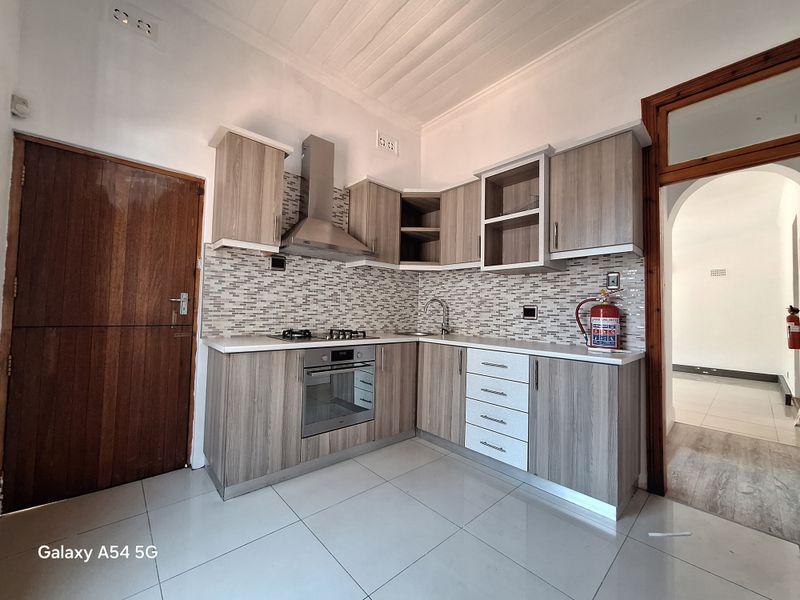 A modern kitchen featuring wood-grain cabinetry, a built-in oven, gas hob, stainless steel extractor fan, and a mosaic tile backsplash.