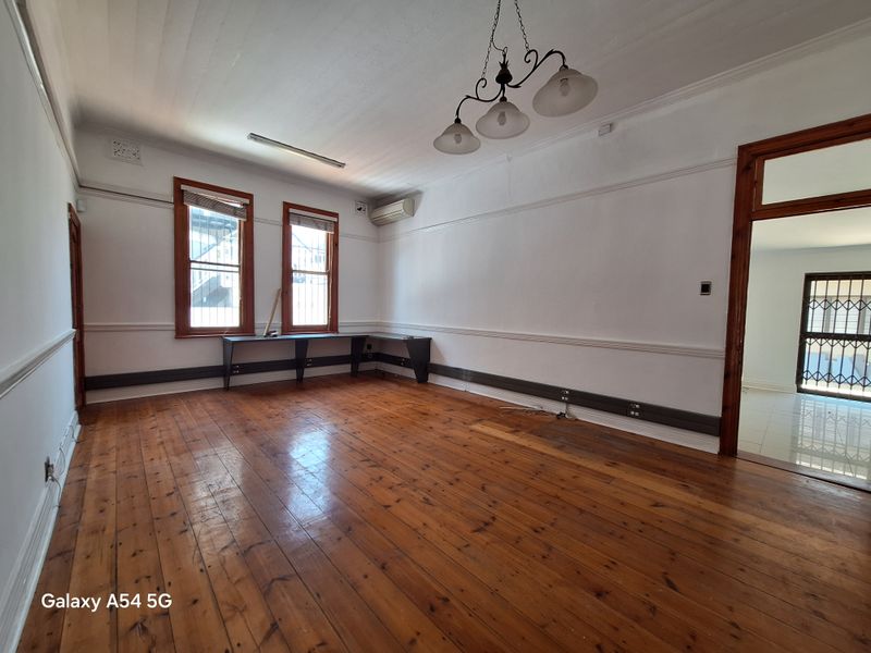 Spacious office area featuring polished timber flooring, built-in desk space, wall-mounted air conditioning unit, and classic crown molding.