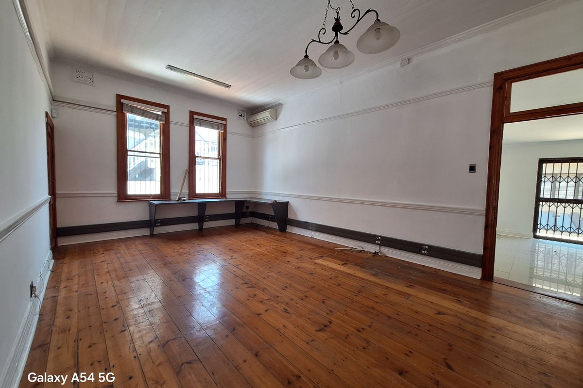 Spacious office area featuring polished timber flooring, built-in desk space, wall-mounted air conditioning unit, and classic crown molding.