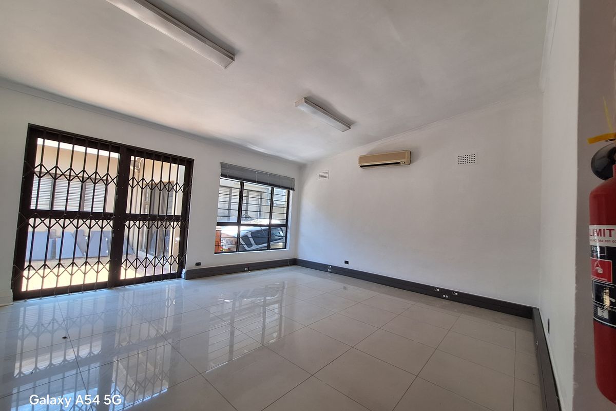 A bright, open-plan office space featuring polished tile flooring, security gates, and a wall-mounted air conditioning unit.
