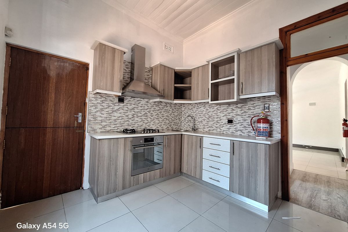 A modern kitchen featuring wood-grain cabinetry, a built-in oven, gas hob, stainless steel extractor fan, and a mosaic tile backsplash.