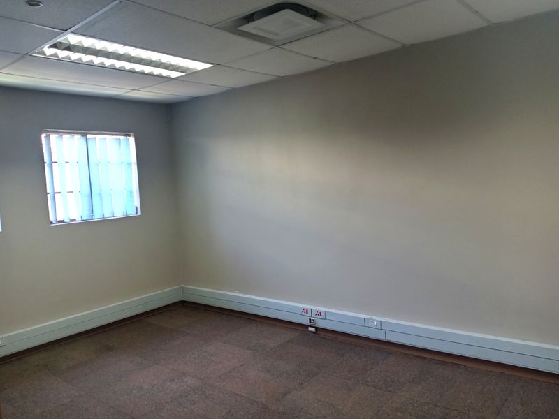 A vacant office space featuring a suspended ceiling with recessed lighting, vertical window blinds, and perimeter trunking for electrical and data connectivity.