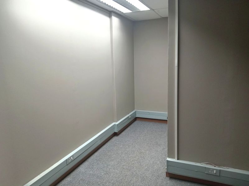A vacant office space featuring neutral wall tones, grey carpeting, and integrated perimeter trunking for electrical and data connectivity.