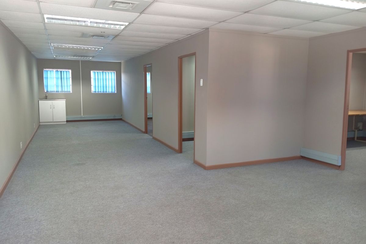 An open-plan office space featuring a suspended ceiling with recessed lighting, carpeted flooring, and multiple partitioned doorways.