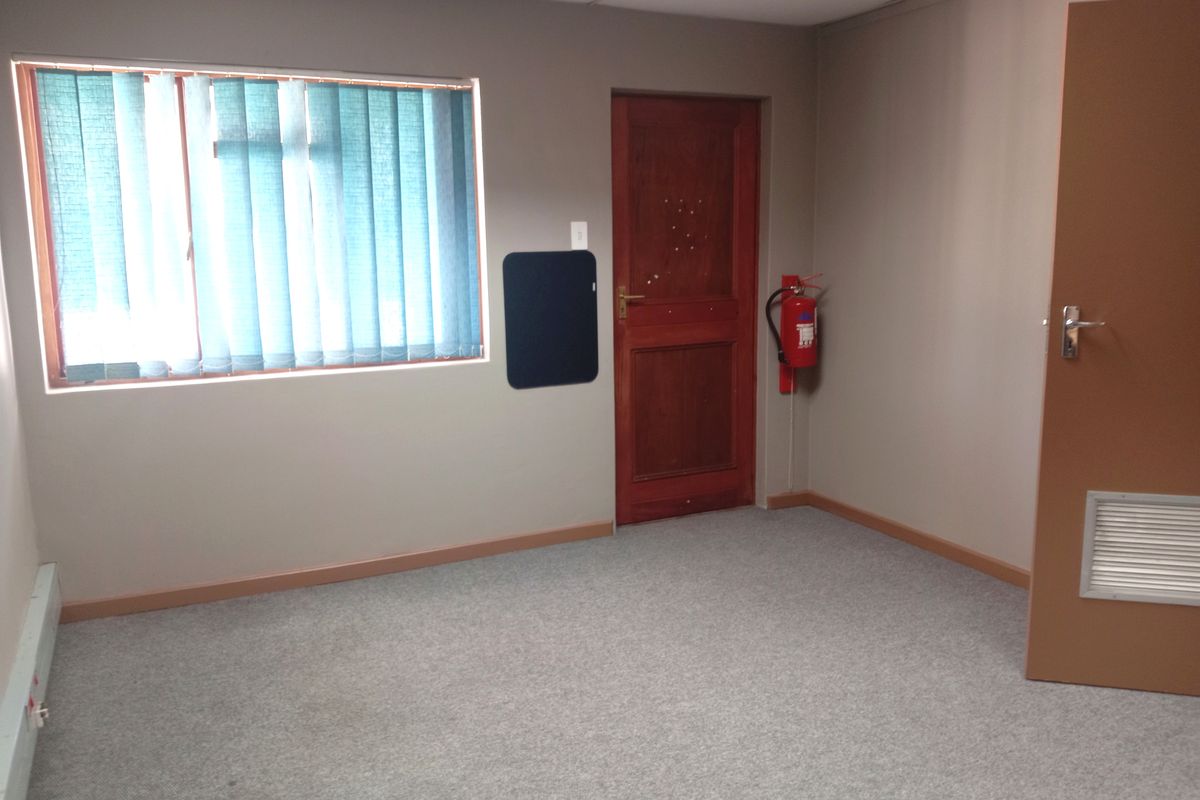 A functional office space featuring neutral walls, carpeted flooring, a wooden door, and a wall-mounted fire extinguisher.