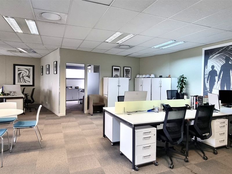 A professional open-plan office space featuring carpet tiles, suspended ceilings with recessed lighting, and integrated storage cabinetry.