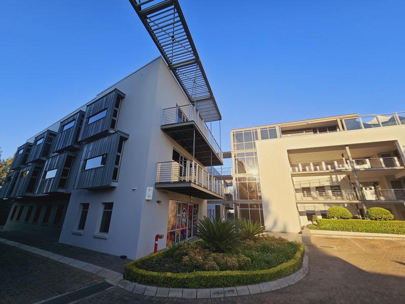 Modern multi-story office building featuring contemporary metal cladding, integrated balconies with metal railings, and a landscaped entrance area.