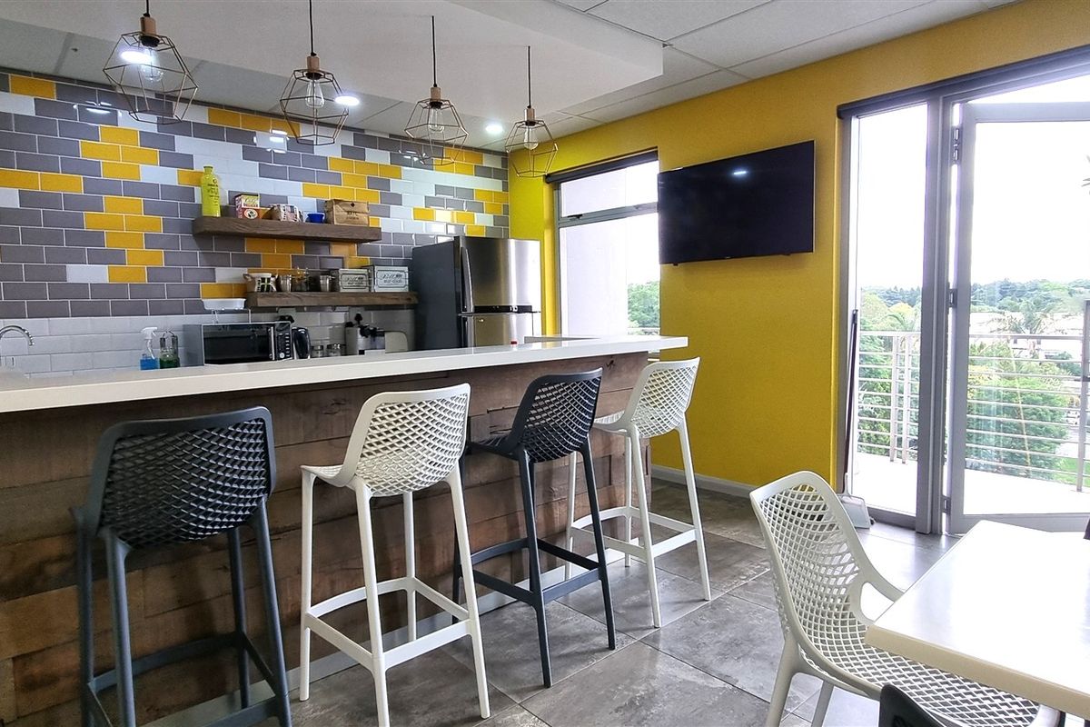 Modern office kitchen area featuring a breakfast bar, stylish tiled backsplash, pendant lighting, and direct access to a balcony through sliding glass doors.