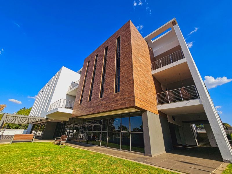 Modern office building exterior featuring a combination of wood-look cladding, large glass windows, and multi-level balconies overlooking a landscaped lawn.