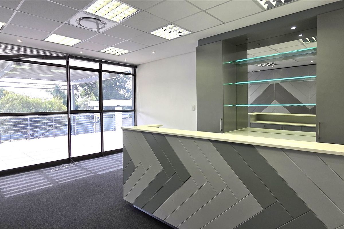 Modern office space featuring a custom built-in reception desk, sleek cabinetry, suspended ceiling with recessed lighting, and large glass doors leading to an outdoor area.