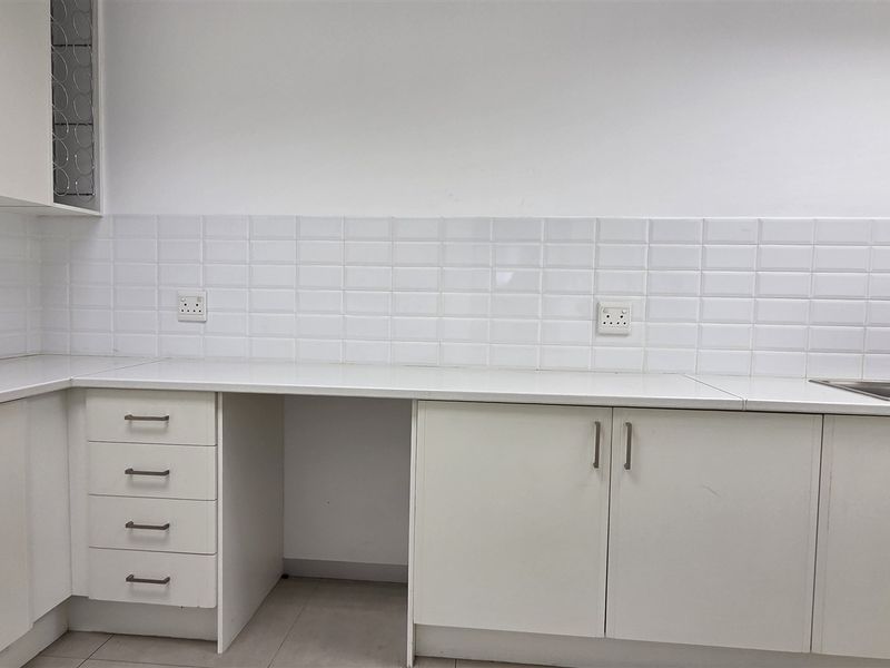 A clean, functional kitchenette featuring white built-in cabinetry, subway tile backsplash, and a stainless steel sink with ample counter space.