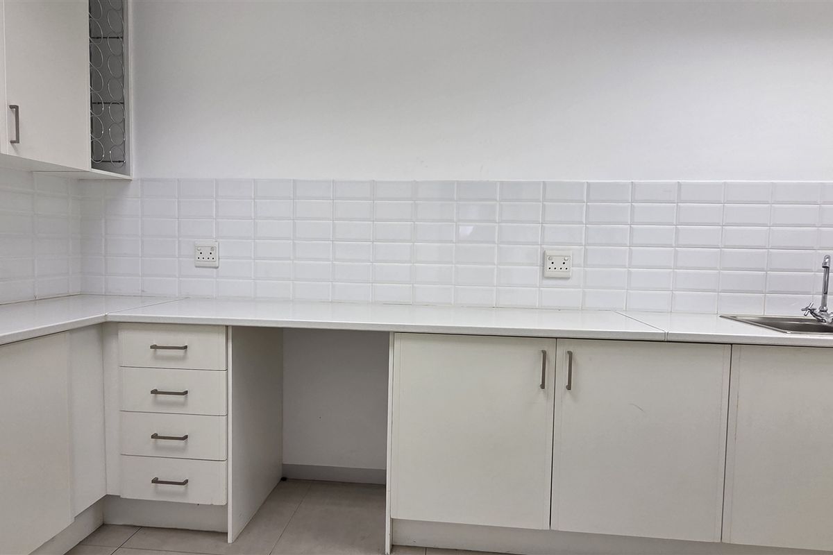 A clean, functional kitchenette featuring white built-in cabinetry, subway tile backsplash, and a stainless steel sink with ample counter space.