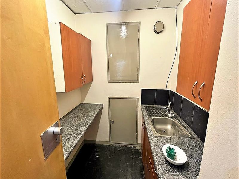 A compact office scullery area featuring built-in cabinetry, granite countertops, and a stainless steel sink with tiled backsplash.