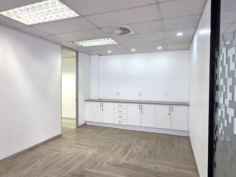 A clean, modern office space featuring herringbone-patterned laminate flooring, built-in storage cabinetry, and a contemporary frosted glass partition.