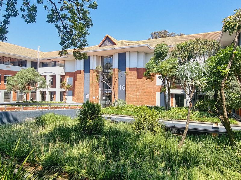 A well-maintained multi-story office building featuring a classic brick facade, tiled roof, and established landscaped gardens at the entrance.
