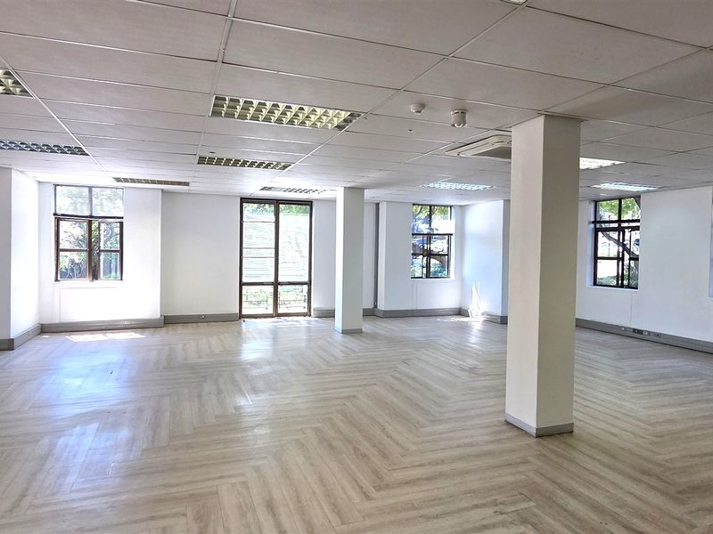 Spacious open-plan office area featuring herringbone flooring, suspended ceilings with recessed lighting, and large windows providing ample natural light.