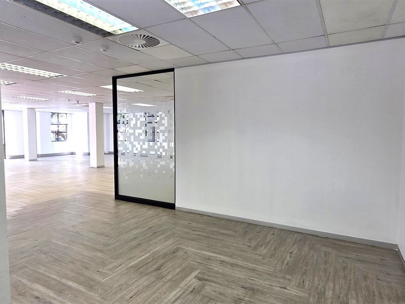 A bright, open-plan office space featuring modern herringbone vinyl flooring, a glass partition, and a suspended ceiling with recessed lighting.