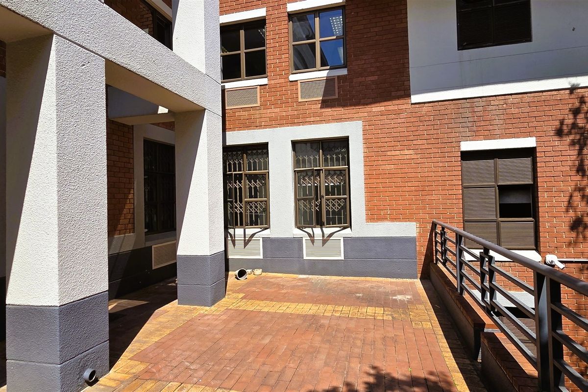A paved outdoor terrace area featuring brick facade walls, metal security bars on windows, and protective metal railings.