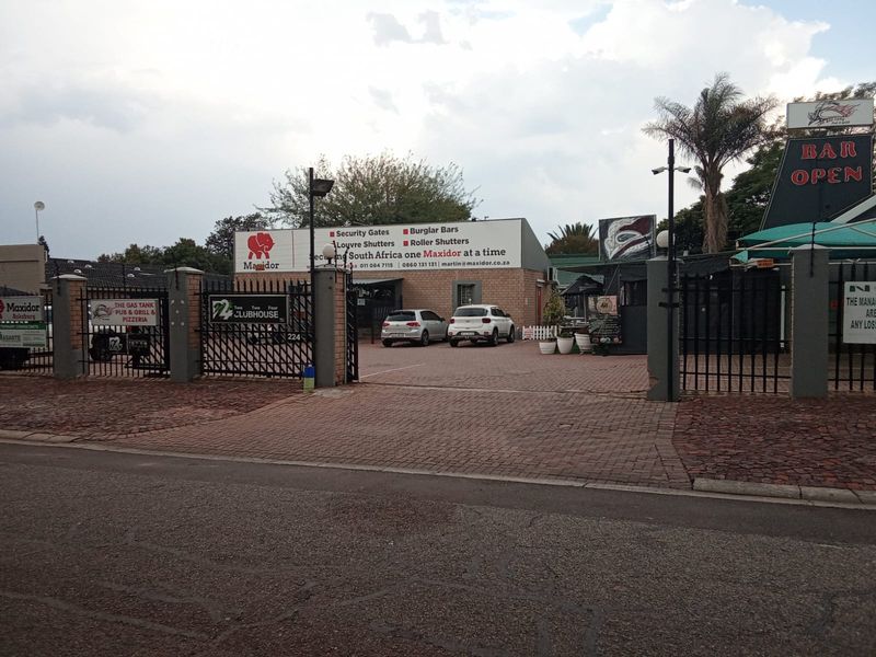 Front exterior view of a commercial property featuring a paved driveway, secure gated entrance, and prominent business signage.