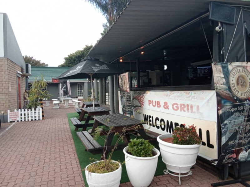 Outdoor pub and grill seating area featuring a covered bar structure, paved patio, and casual dining space.